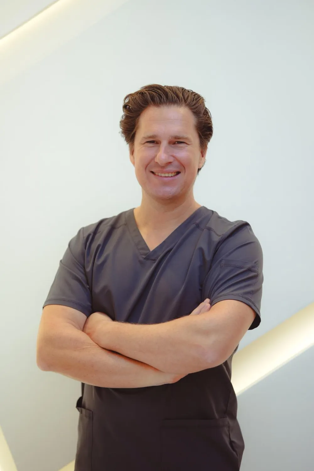Dr. Christian Wolf in grey scrubs, standing with arms folded in the clinic
